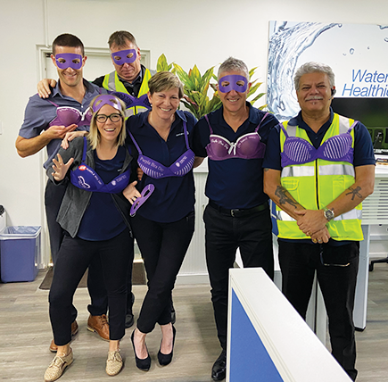 Team photo wearing purple bras in recognition of Purple Bra Day